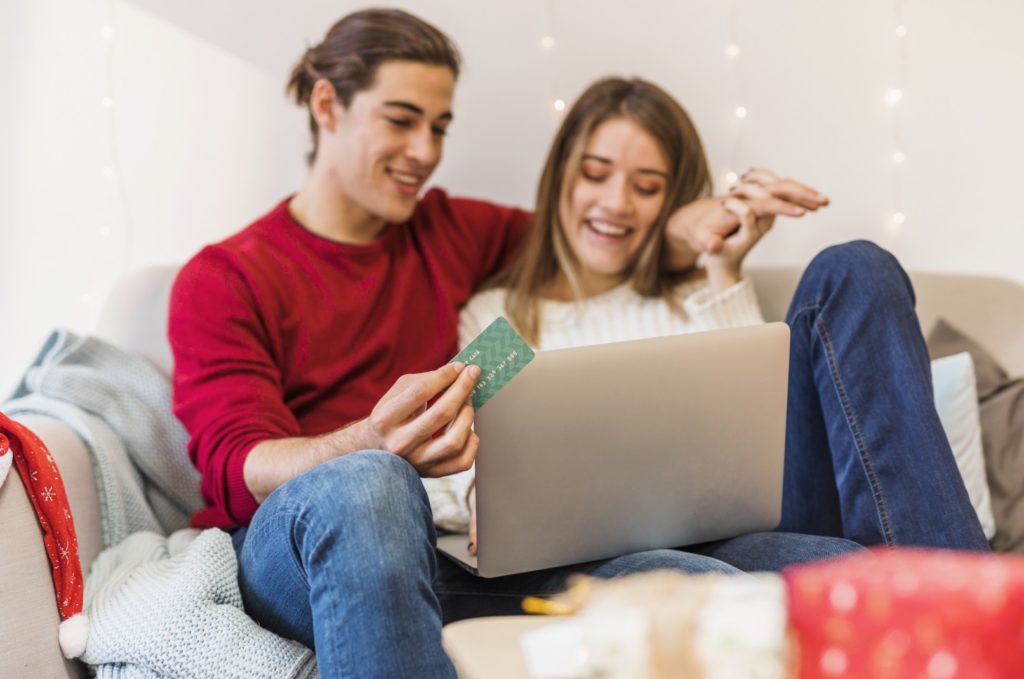 Ein glückliches Paar mit Kreditkarte in der Hand vor einem Laptop will gerade in einem Onlineshop bestellen