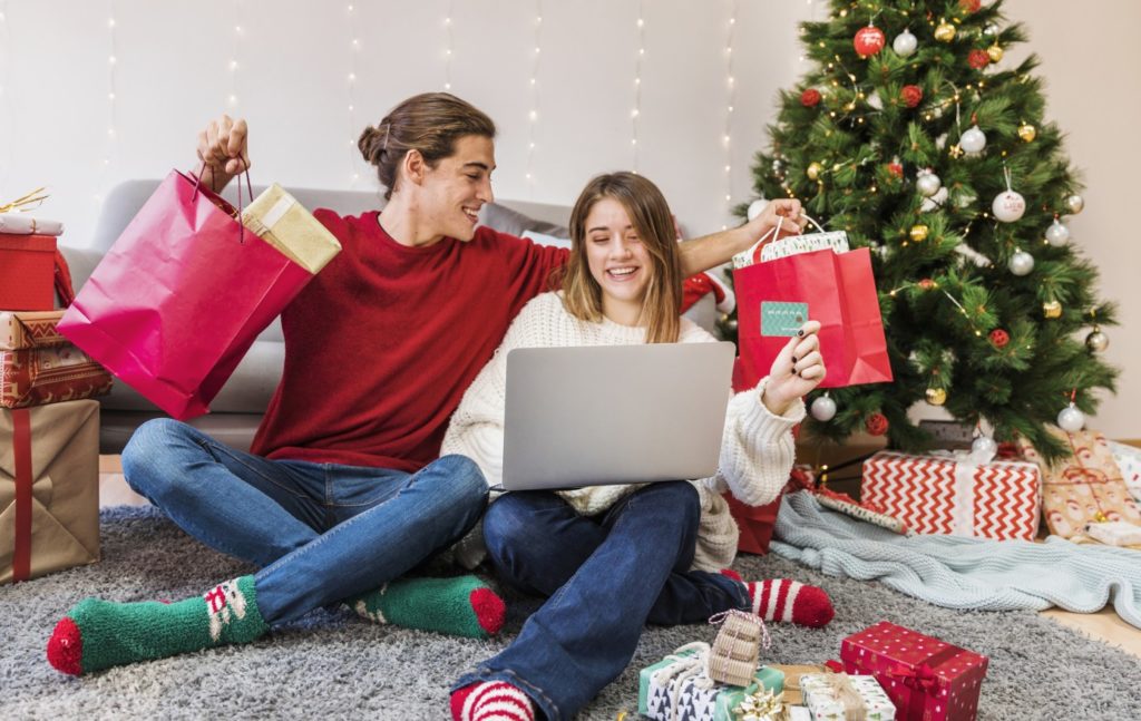 Ein glückliches Paar mit Kreditkarte in der Hand vor einem Laptop mit Geschenken aus einem Onlineshop in ihren Händen