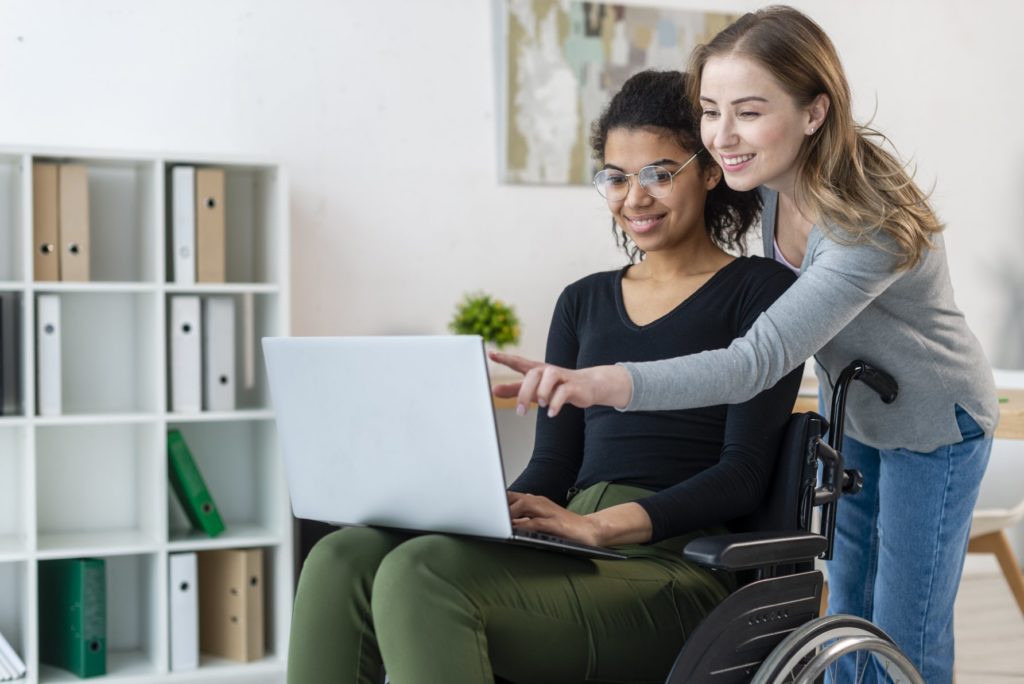 Eine Frau im Rollstuhl nutzt gemeinsam mit ihrer Freundin das Internet