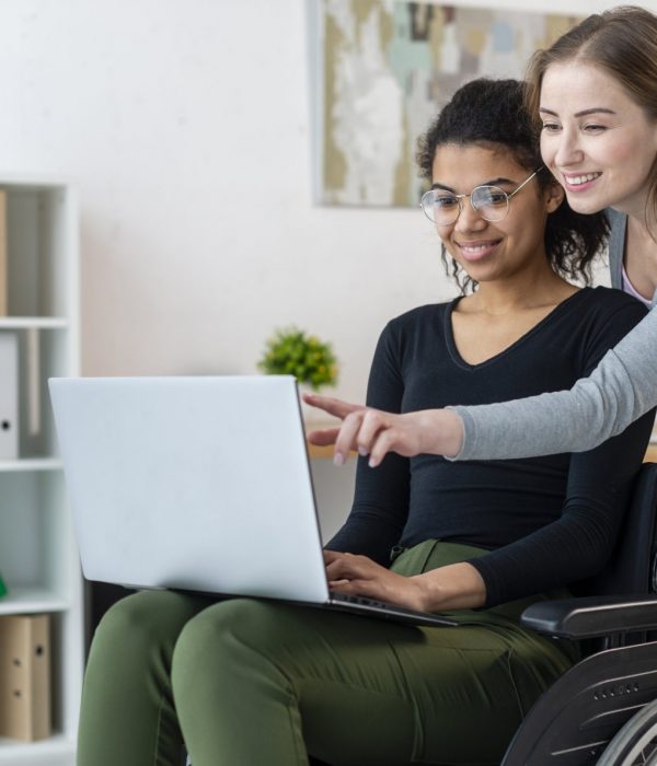 Eine Frau im Rollstuhl nutzt gemeinsam mit ihrer Freundin das Internet